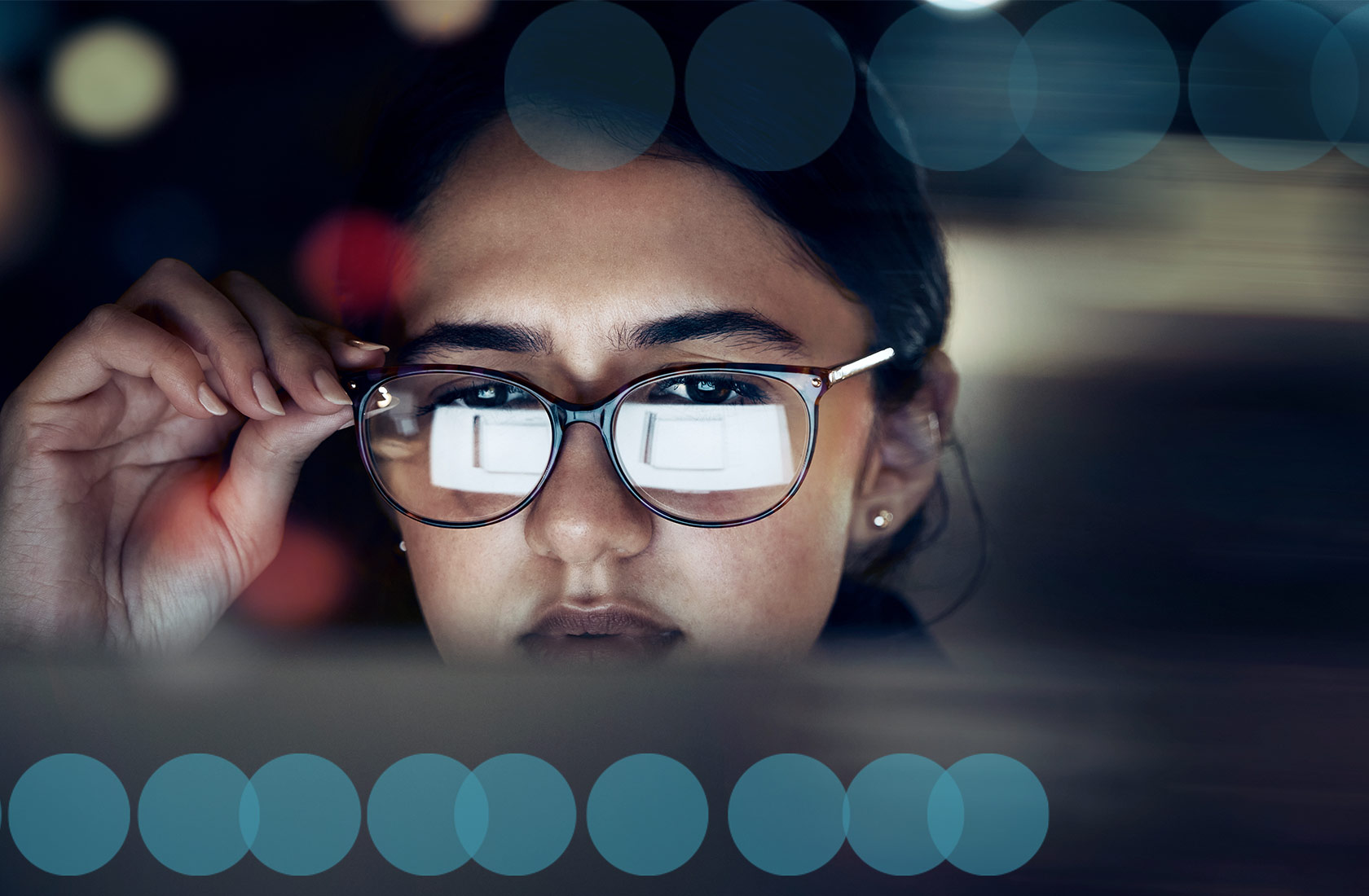 A young woman looks at a computer monitor, the screen reflects off her glasses